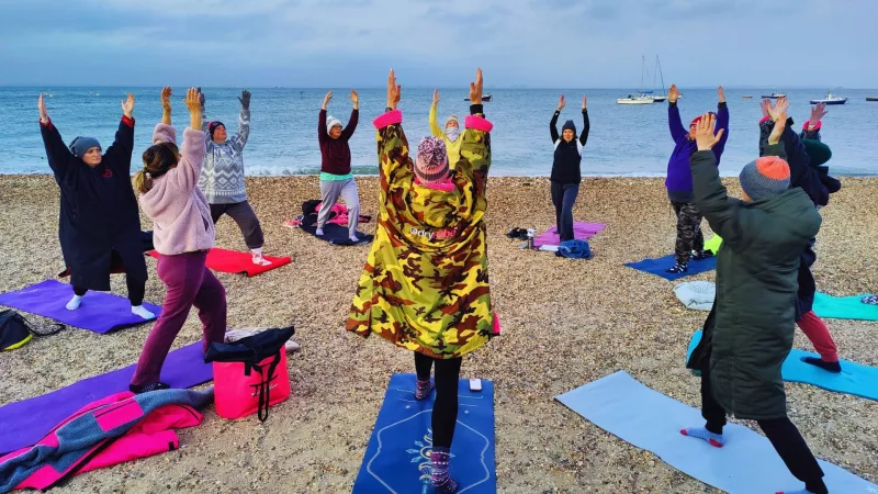 Group of people on a beach doing yoga as part of YogaSwim